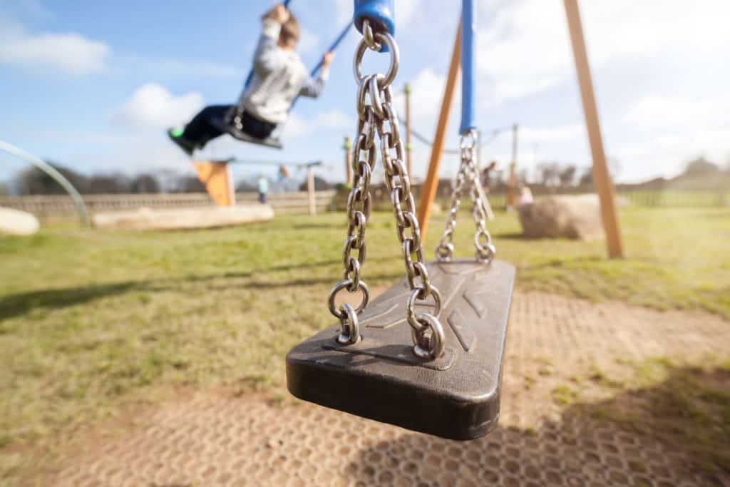 Empty playground swing with children playing in the background c