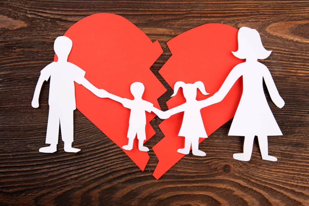 Paper cutout silhouette of a family split apart on a paper heart