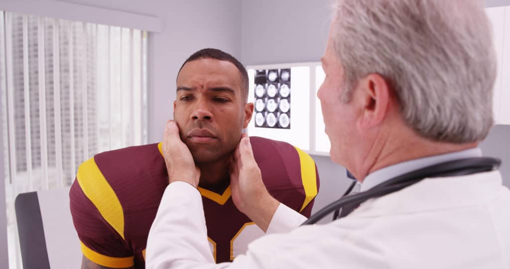 College football player having senior doctor review his concussion injury.