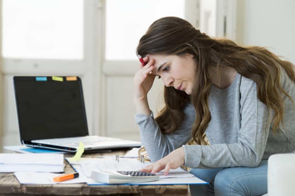 young attractive and desperate woman suffering stress doing domestic accounting paperwork bills and invoices worried and stressed at home sofa couch with laptop computer and bank receipts