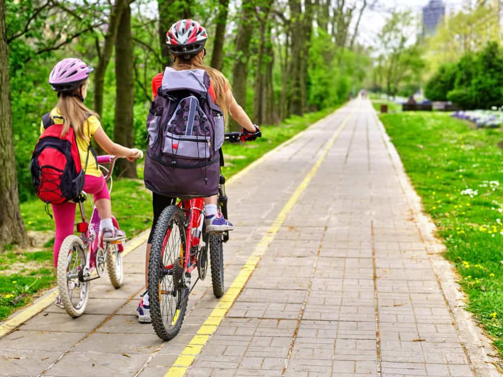 Bikes bicyclist girl. Girls wearing bicycle helmet with rucksack ciclyng bicycle. Girls children cycling on yellow bike lane. Bike share program save money and time. Back view.