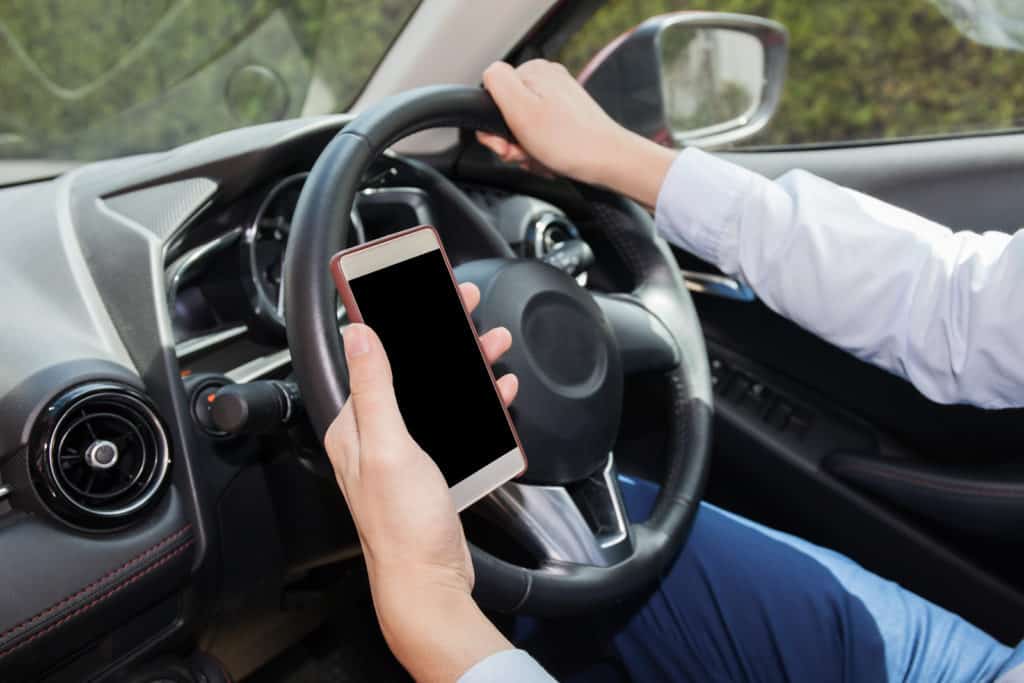 Businessman checking phone while careless driving - distraction and bad habit driving concept - with clipping mask on screen