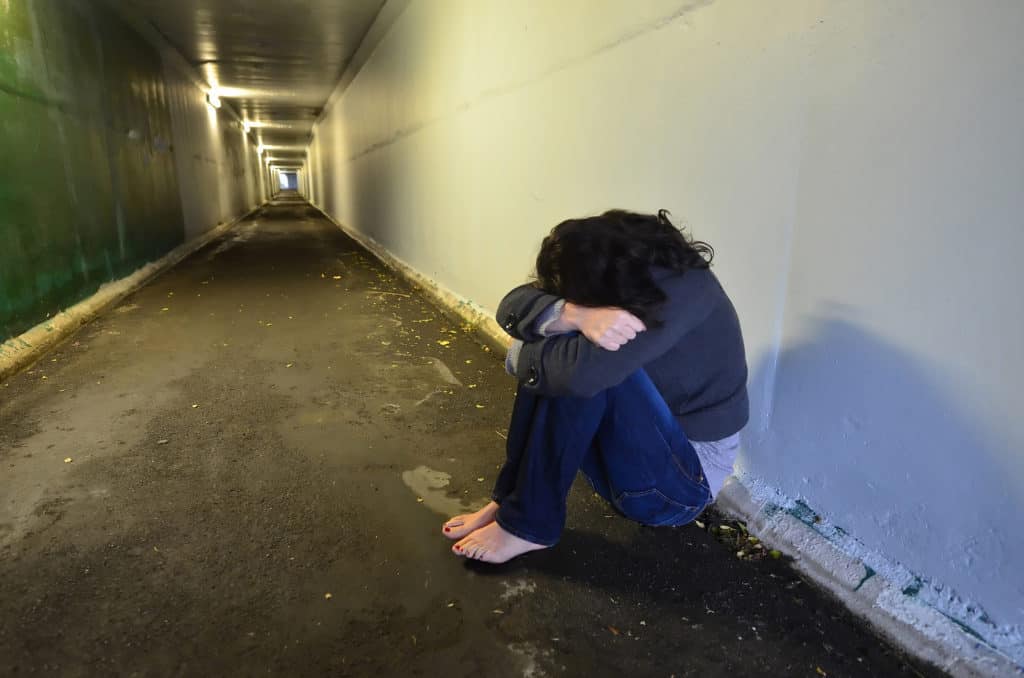 Crime scene concept photo of rape victim. A sad woman sits on the floor of a dark tunnel.