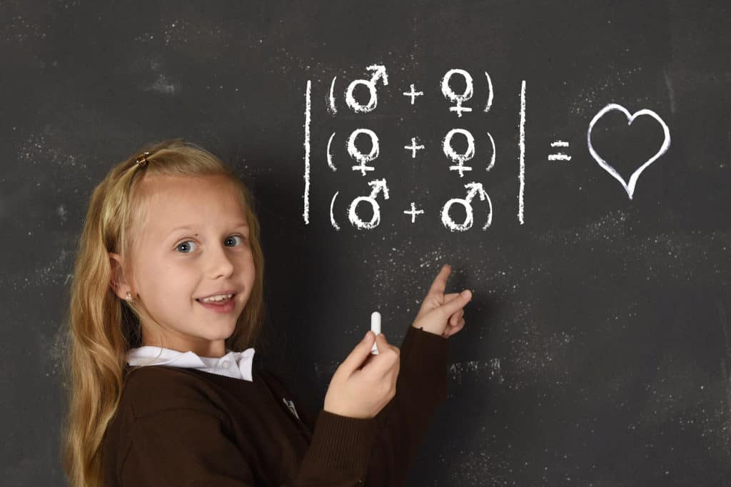 young beautiful blond sweet schoolgirl in uniform holding chalk writing on blackboard standing for freedom of sexuality orientation supporting love for heterosexual and homosexual couples