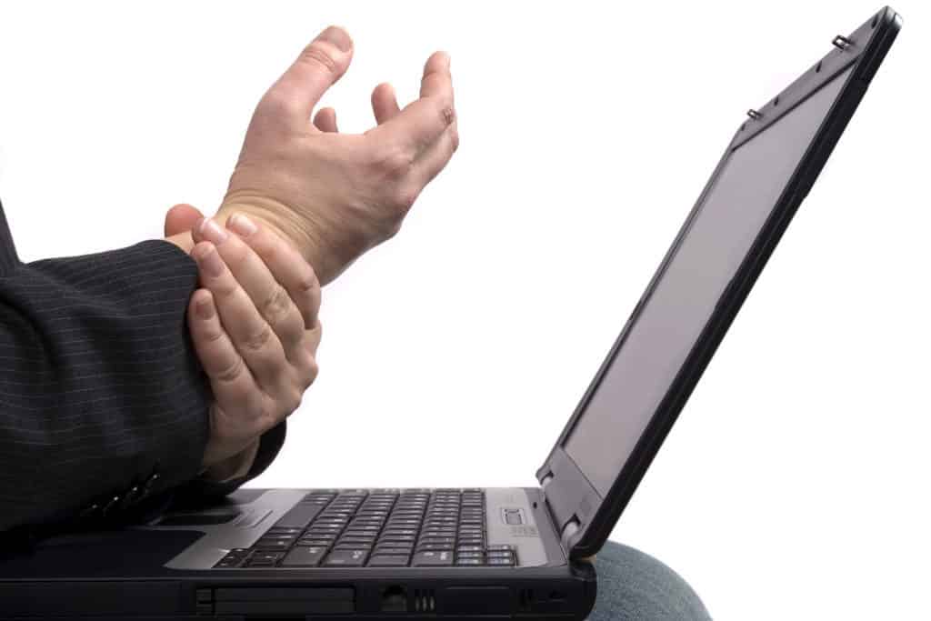 a business man holding his hands because of pain while working on a laptop.