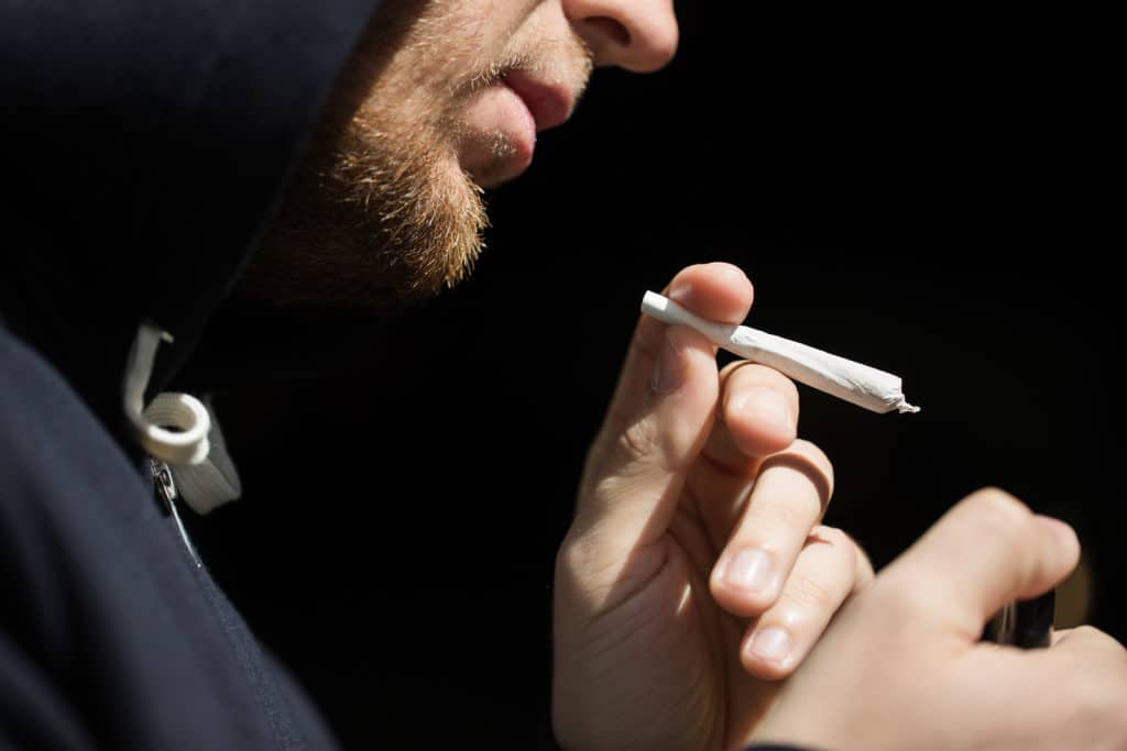 drug use, substance abuse, addiction, people and smoking concept - close up of addict lighting up marijuana joint with lighter