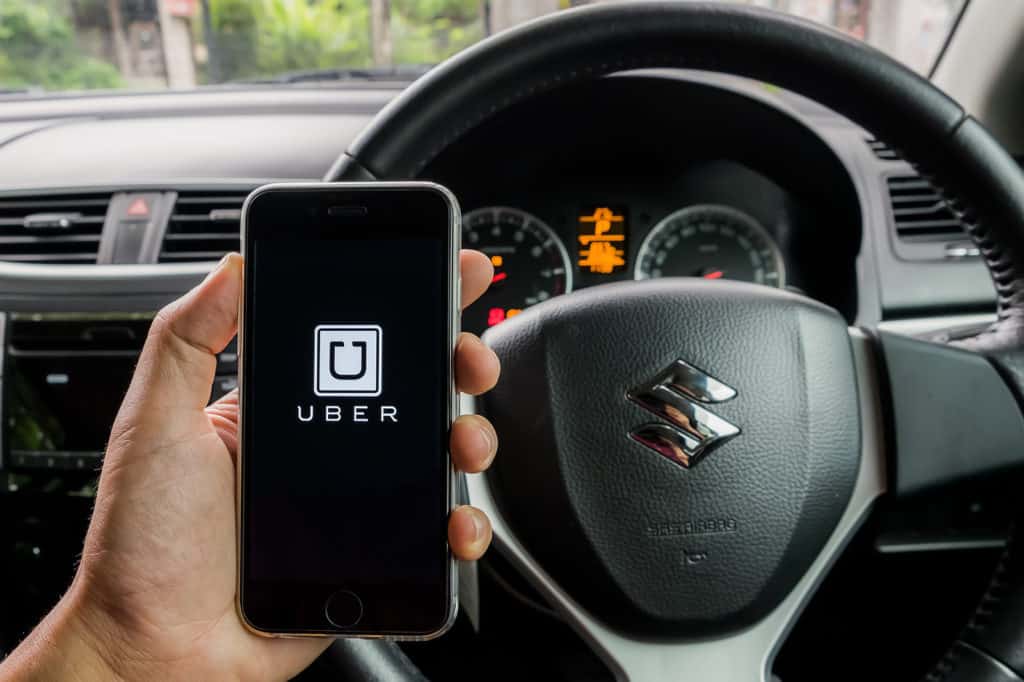 CHIANG MAITHAILAND - JULY 292016 : A MAN hand holding Uber app showing on iphone 6s. Uber is smartphone app-based transportation network in suzuki swift eco car.