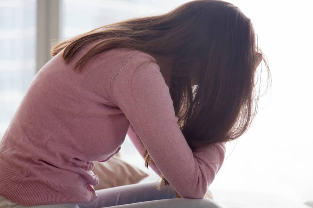 Young depressed woman sitting alone holding her head in hands, sad girl, problems at work, troubles in relationships, unwilling pregnancy, feeling guilty and stressed, tired of being lonely