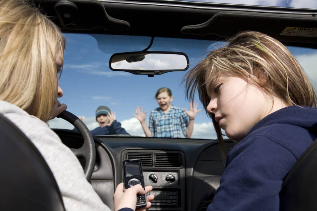 Two teenagers being distracted by a cell phone text instead of watching the road. They are about to hit a boy and girl crossing infront of the car.