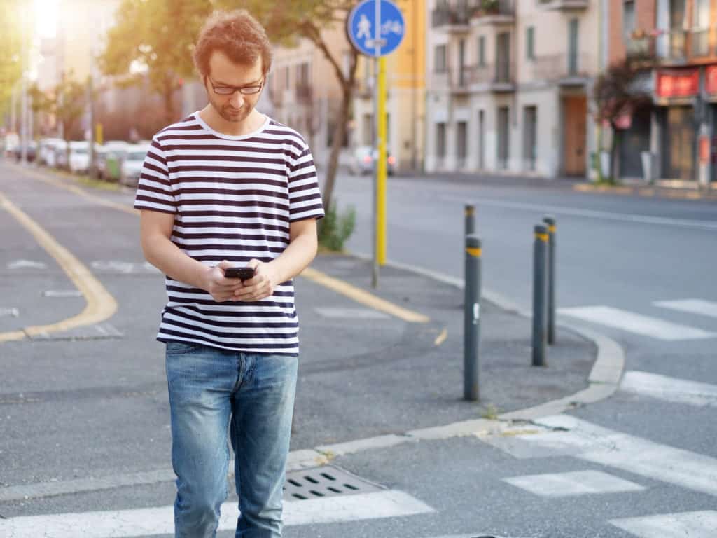 portrait of young adult man crossing inattentively the street distracted by his phone