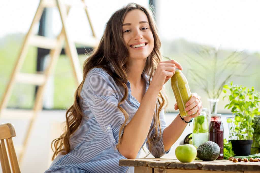 Beautiful happy woman sitting with drinks and healthy green food at home. Vegan meal and detox concept