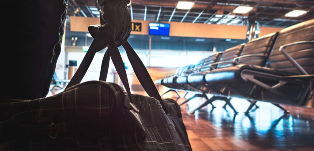 Terrorist in airport planning a bomb attack. Terrorism and security threat concept. Suspicious dangerous man in the shadows with black bag. Gate, bench and waiting area in the blurred background.