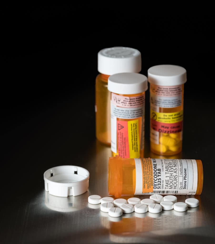 Oxycodone is the generic name for a range of opoid pain killing tablets. Prescription bottle for Oxycodone tablets and pills on metal table for opioid epidemic illustration