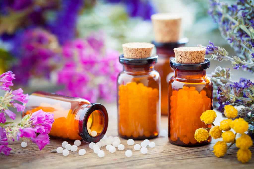 Bottles of homeopathic globules and healing herbs and flowers. Homeopathy medicine.