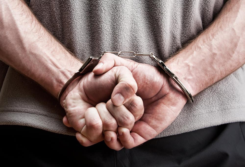 Criminal hands locked in handcuffs. Close-up view