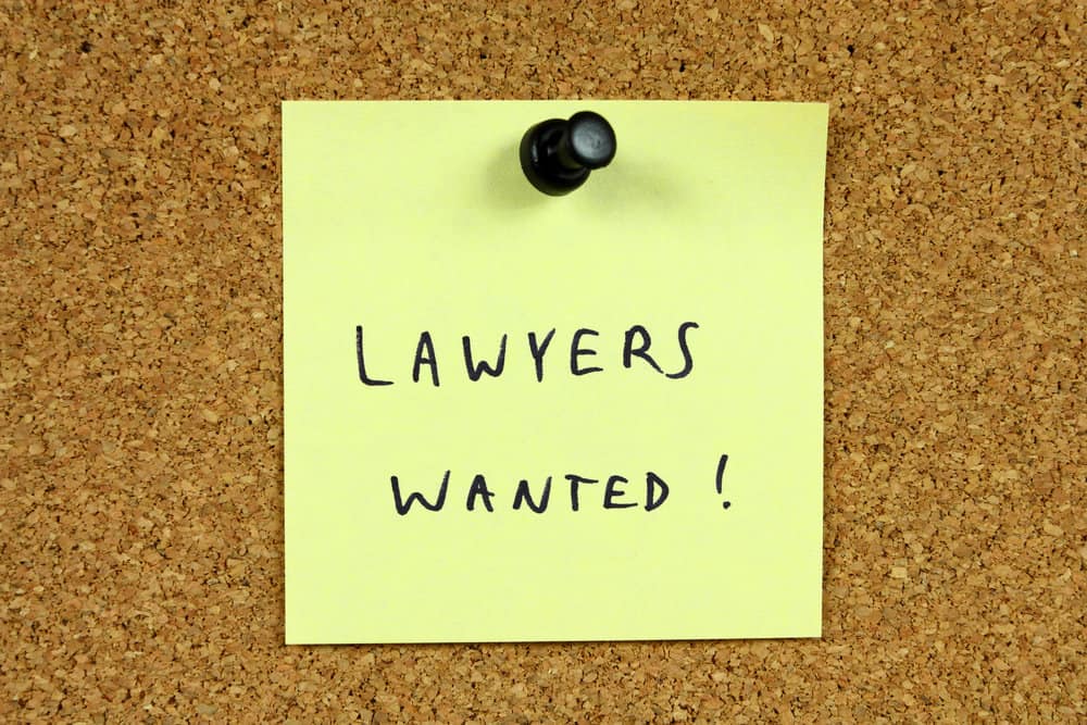 Yellow sticky note pinned to an office notice board. Lawyers wanted - legal career recruitment message.
