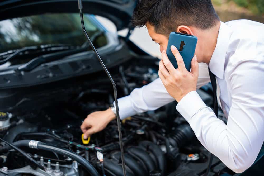 man checking his engine oil and on his phone
