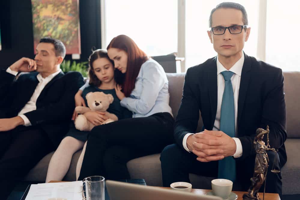 Serious lawyer sits on couch next to upset family. Family in office of family lawyer.