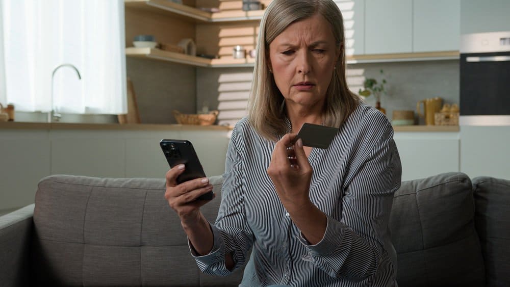 older lady holding credit card and phone looking concerned