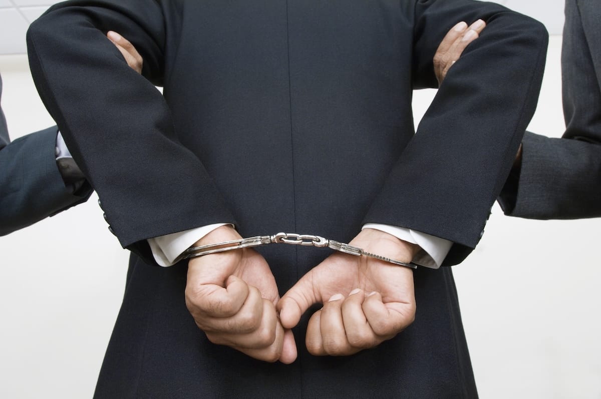 corporate executive in handcuffs and being taken away