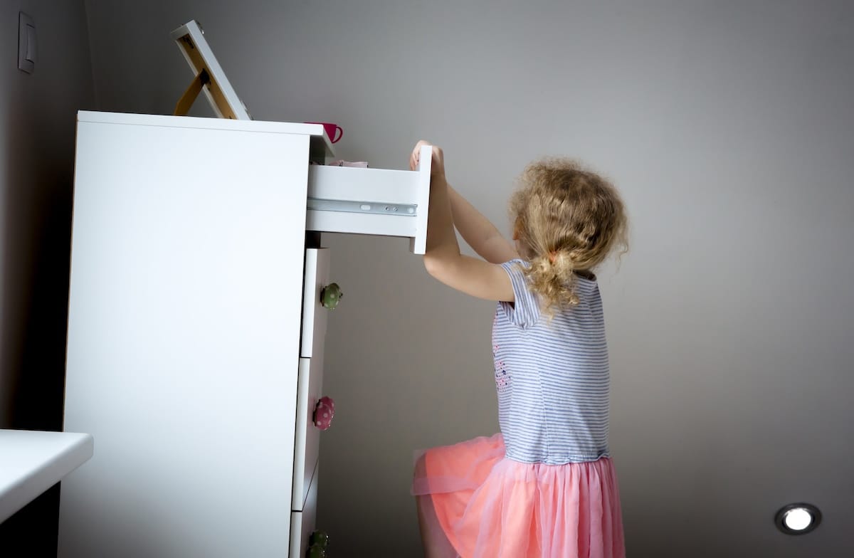 Young child climbing on a dresser drawer, creating a tip-over hazard, illustrating risks from unstable furniture in consumer homes.