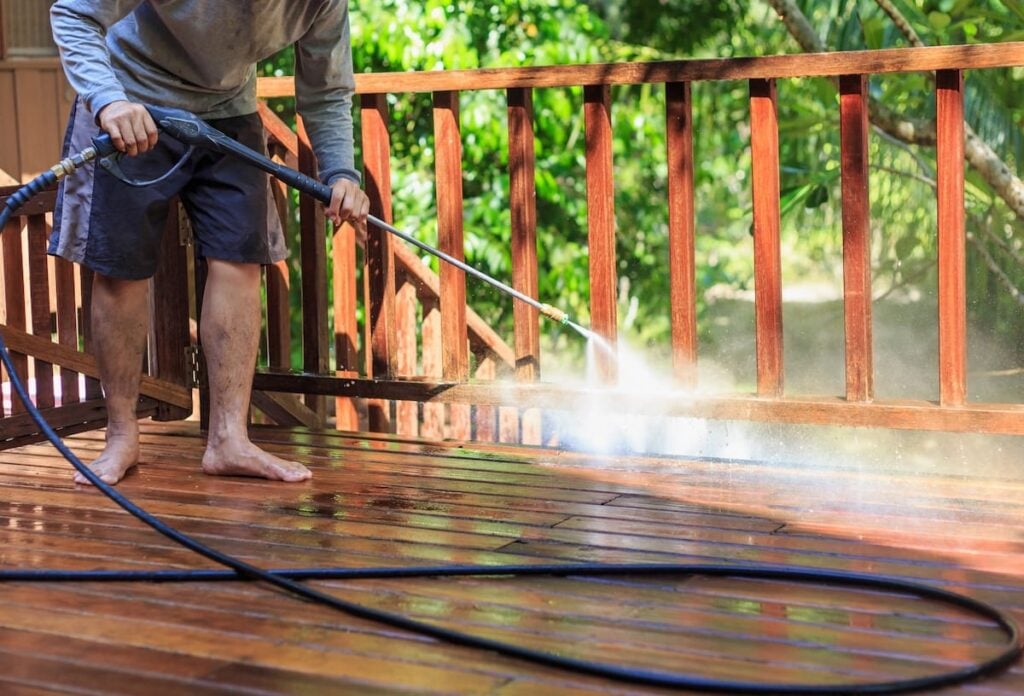 Person using electric pressure washer to clean wooden deck demonstrating typical use before recall