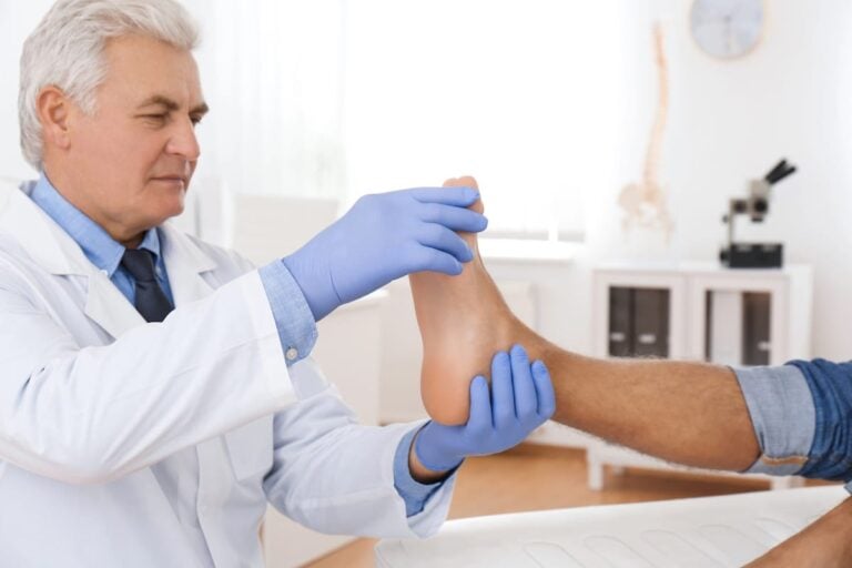 Doctor in blue gloves examining the bottom of a patient's foot in an exam room