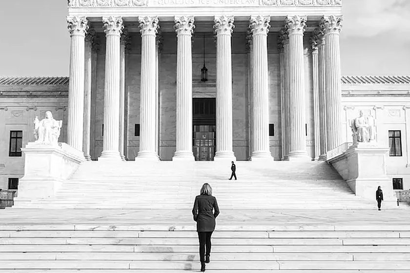 Person walking up the steps of a large columned courthouse, in black and white