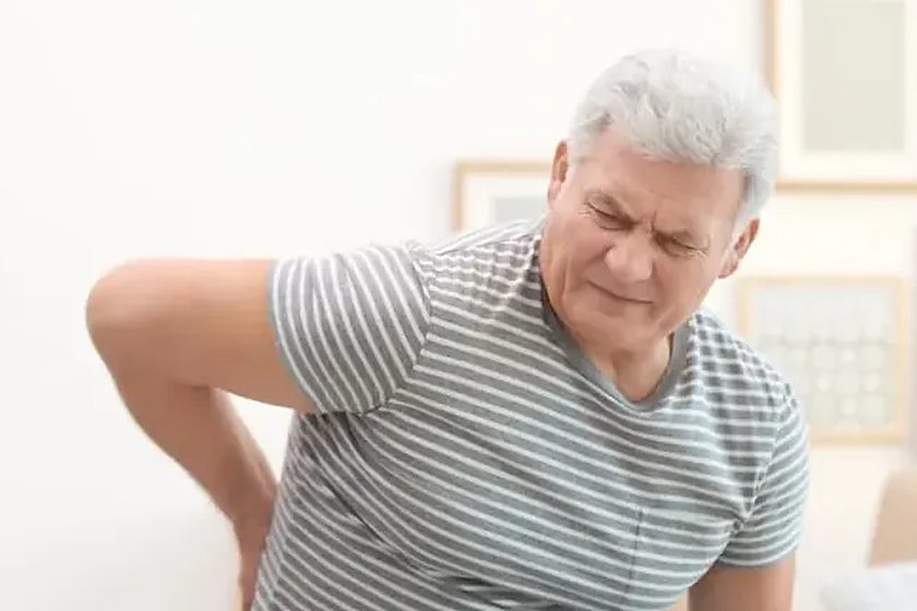 Older man in a striped shirt holding his side in pain