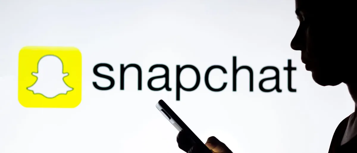 Silhouette of a young woman holding a smartphone in front of the Snapchat logo