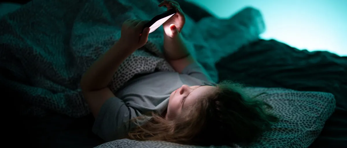 Teen girl lying in bed in a dark room, looking at her smartphone
