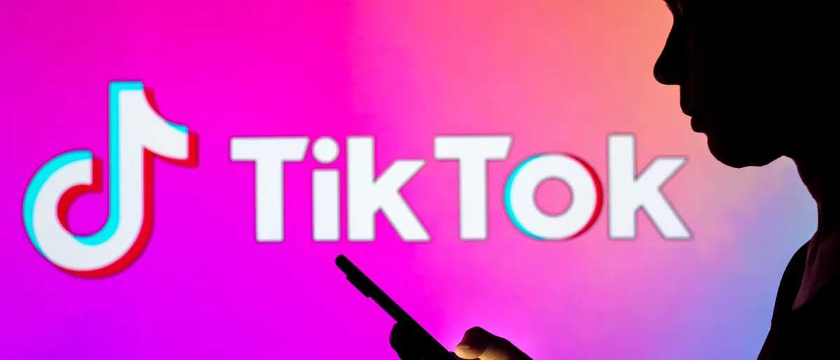Silhouette of a young woman holding a smartphone in front of the TikTok logo